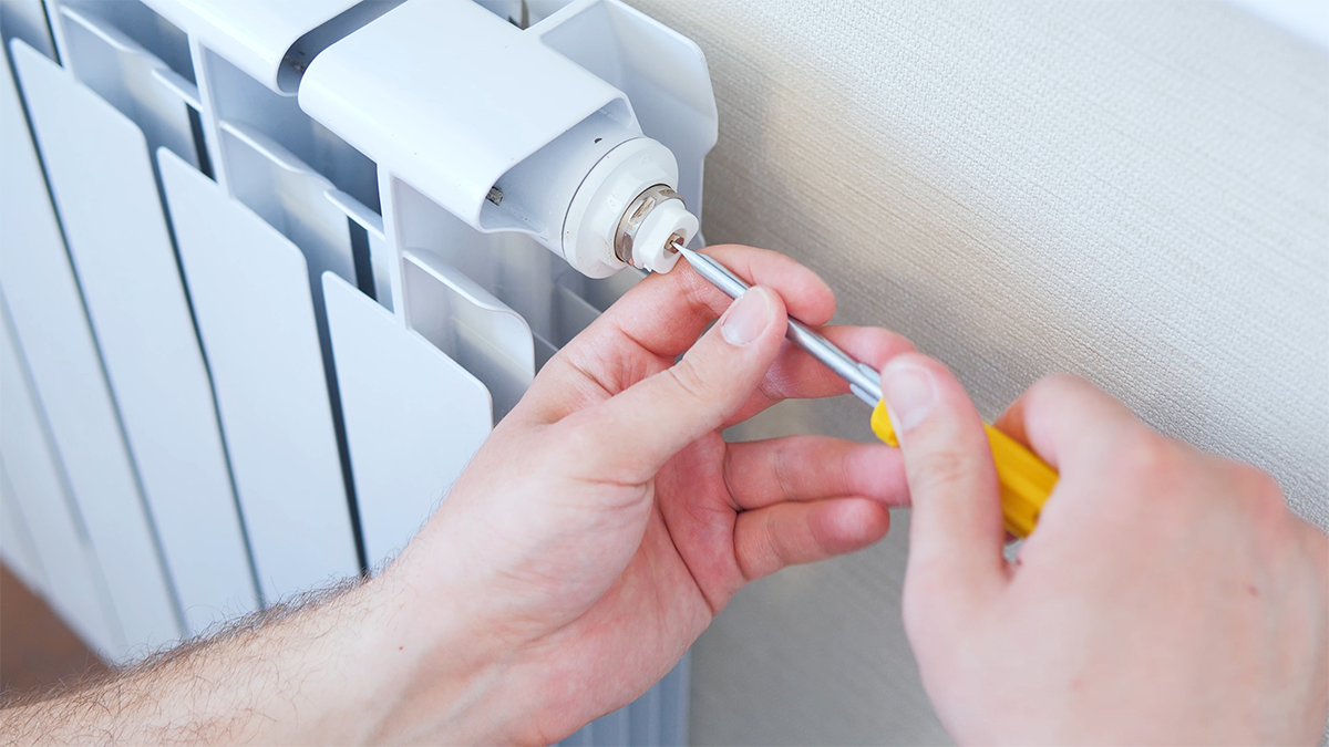 A man bleeding a radiator with a screwdriver
