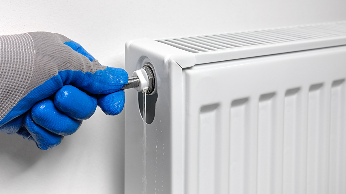 A man draining a radiator with a glove